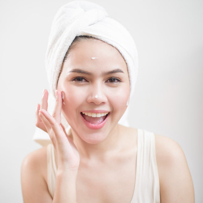 Woman with a towel wrapped around her head, touching her face against a white background